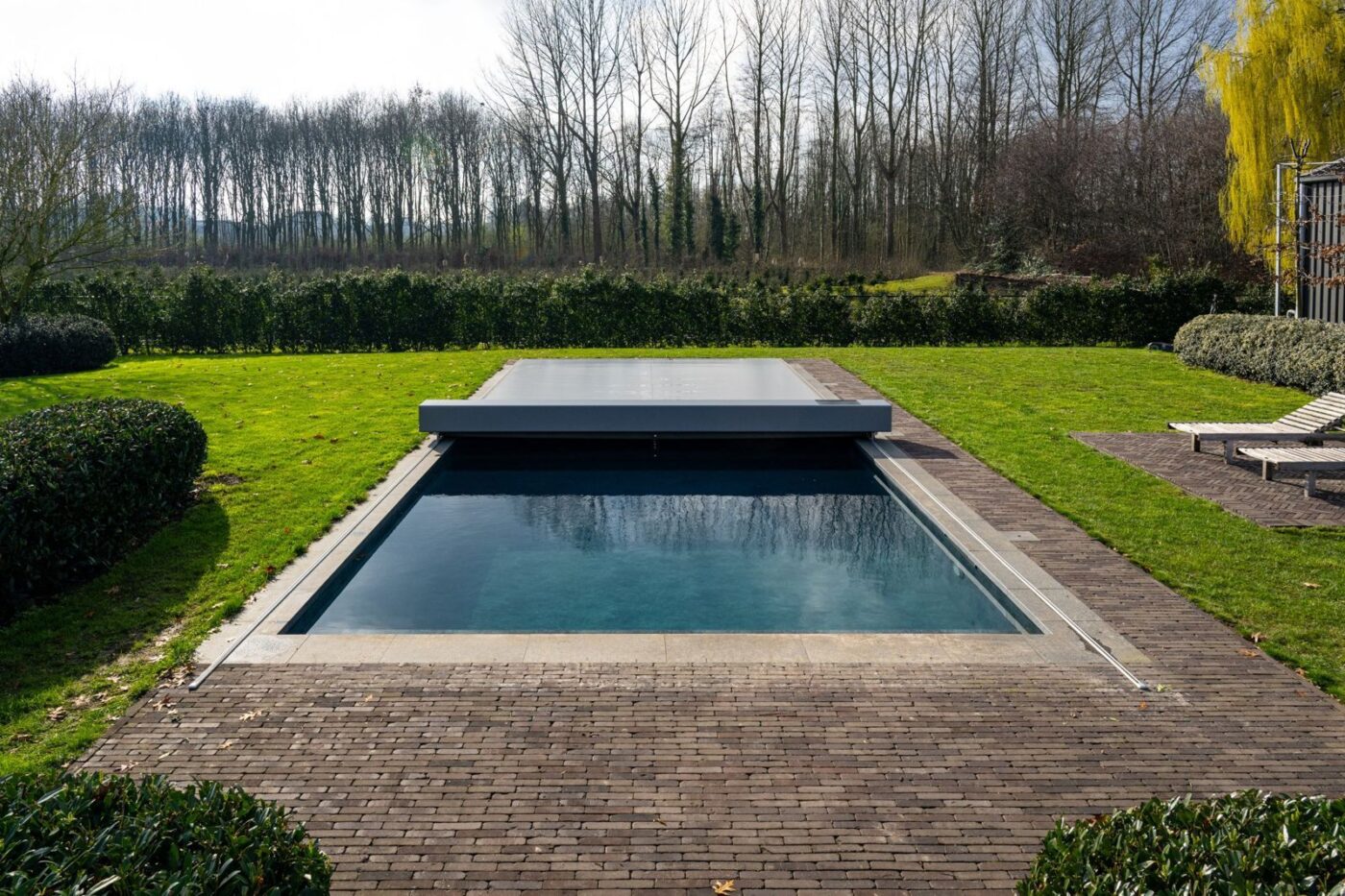 Piscine rectangulaire dans un jardin, couverture Coverseal à moitié ouverte avec son caisson gris